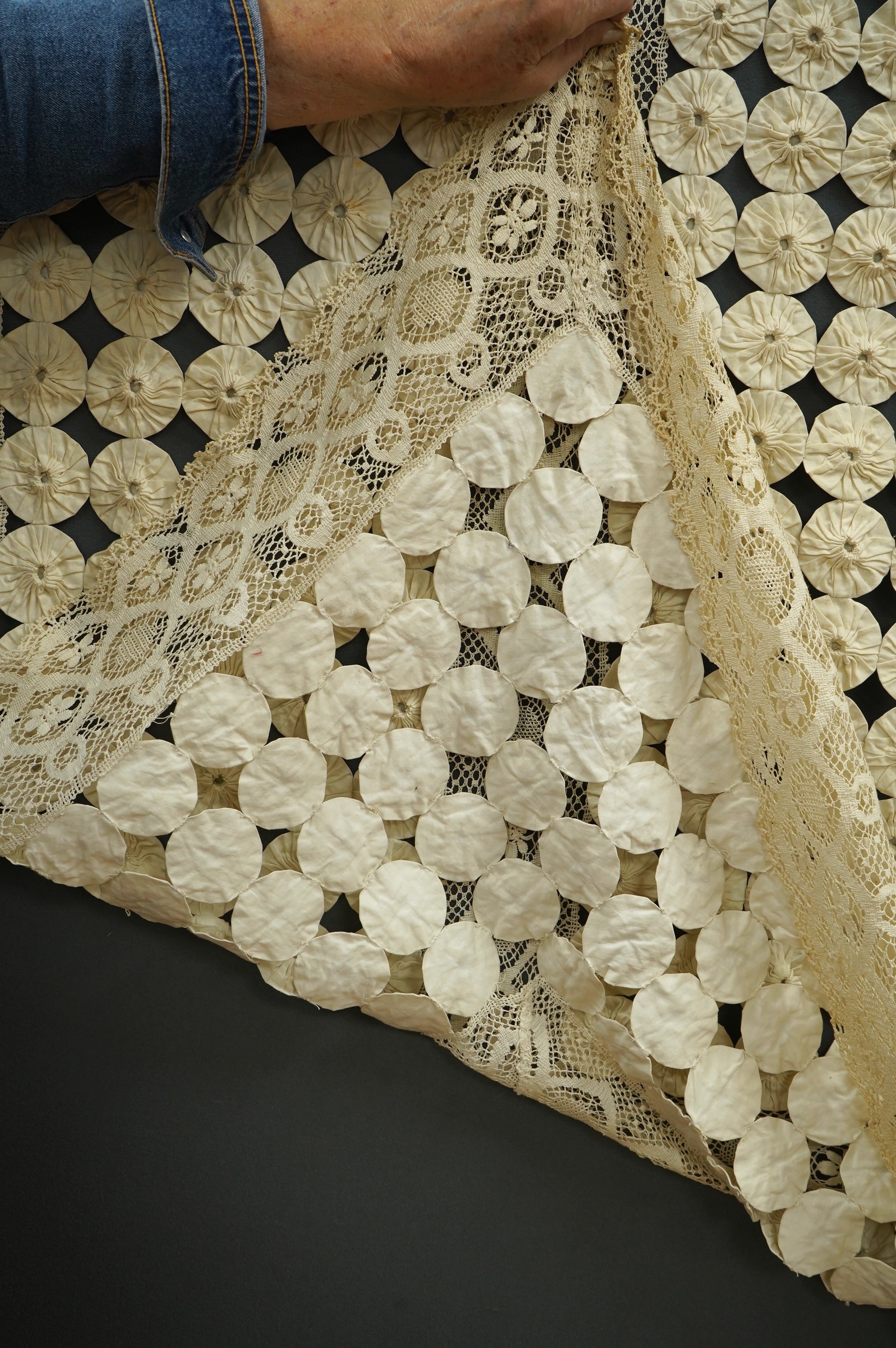 A late 19th early 20th century ‘YoYo’ puffy cream silk and cream bobbin lace quilt/bedcover, made with circles of silk, drawn together as a decorative gathered to top, then stitched together in panels and between wide bo